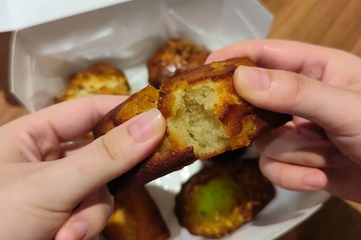 Two hands breaking open a My aunty&rsquo;s bakery orange financier to show the crumb and candied peel