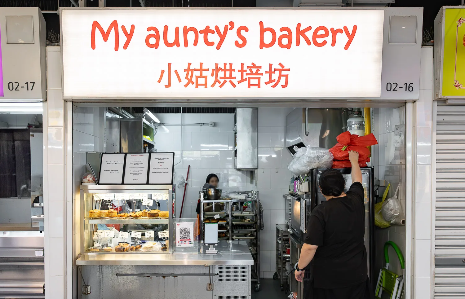 The My aunty&rsquo;s bakery stall front at Market Street Hawker Centre: the lit red-on-white signboard above the display case at unit 02-16