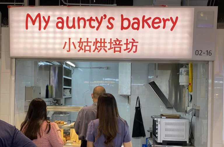 Customers waiting at the My aunty&rsquo;s bakery counter under the lit signboard